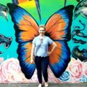 A photo of TCU alumna Laura Patzke posing in front of a butterfly mural.