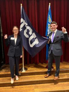 Two students standing with TCU flag and holing up horned frog hand sign