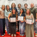 A group of individuals standing together on a red carpet in front of a backdrop featuring the text "Festival of Media Arts" and "BEA." Three individuals in the front are holding certificates.