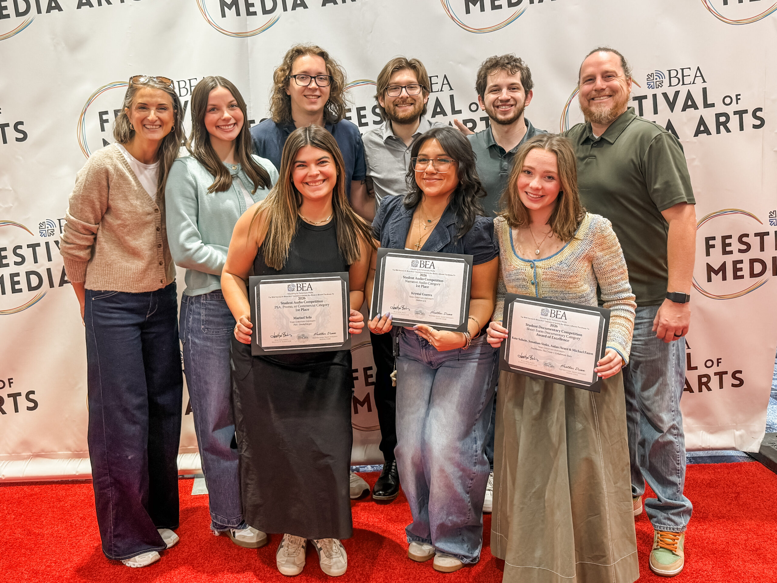 A group of individuals standing together on a red carpet in front of a backdrop featuring the text "Festival of Media Arts" and "BEA." Three individuals in the front are holding certificates.