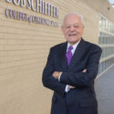 A photo of TCU alumnus Bob Schieffer standing with his arms crossed in front of the building on TCU's campus which bears his name.