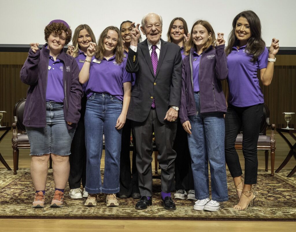A group of female students pose with Bob Schieffer, all with their hands raised in the Go Frogs handsign.
