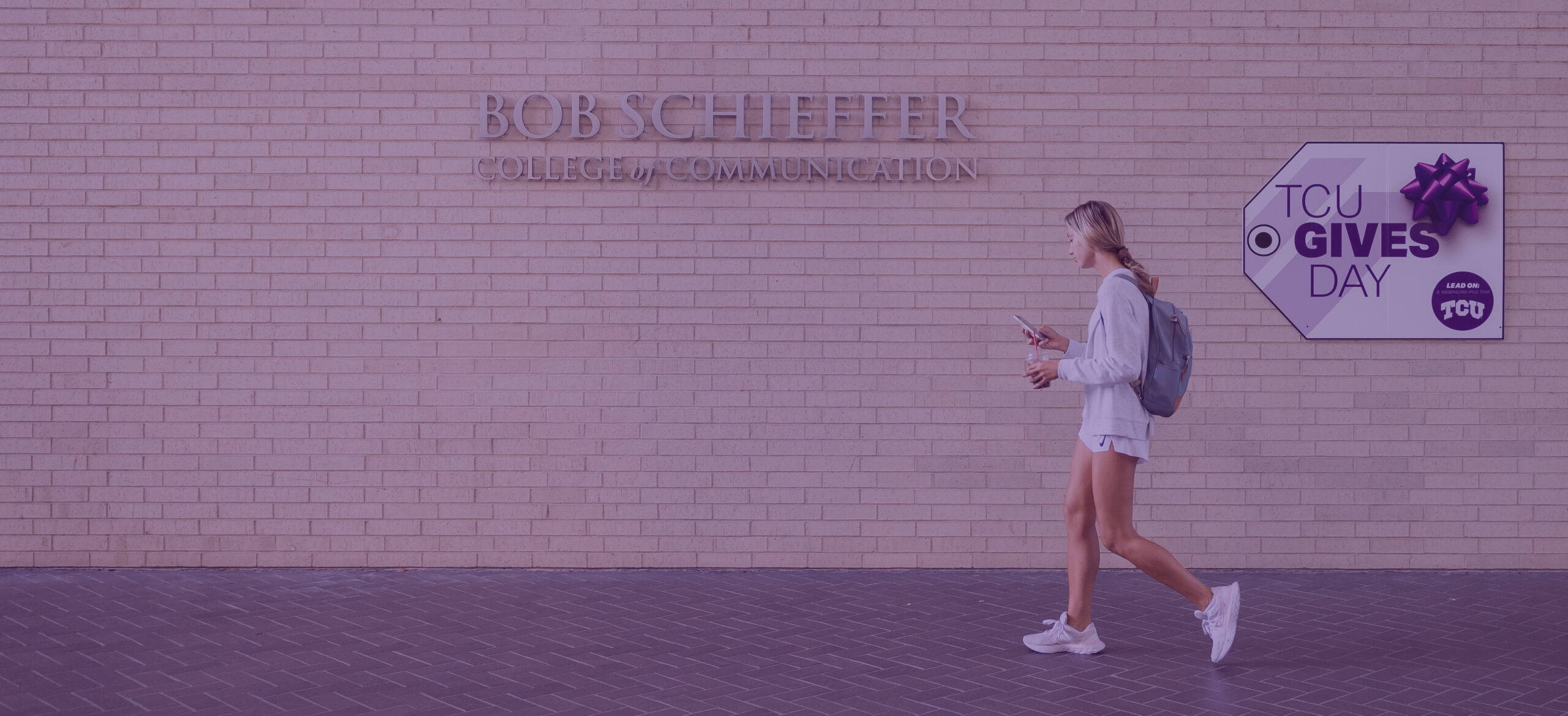 A student walks in front of the Bob Schieffer College of Communication. A large sign behind her proclaims T C U Gives day.