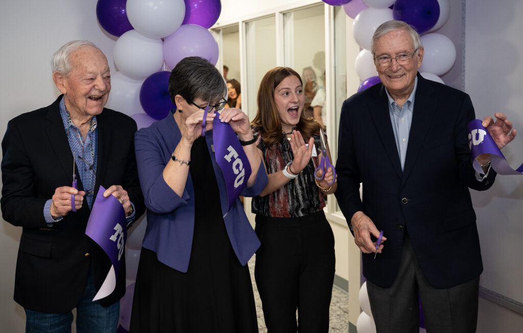 Four people with expressions of joy and excitement hold up sections of a purple TCU ribbon cut during a ribbon-cutting ceremony.
